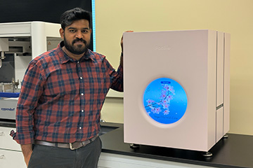 A researcher stands beside a genomic sequencing instrument in a laboratory, highlighting advanced scientific equipment used for genetics and biotechnology research.