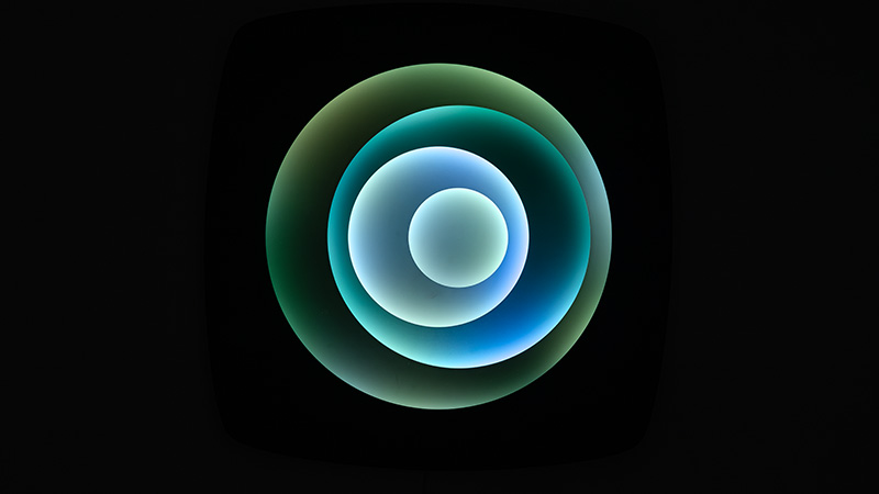 Abstract image showing concentric, softly glowing circular rings in yellow and gold radiating from a blue center, set within a black rounded square on a neutral background.