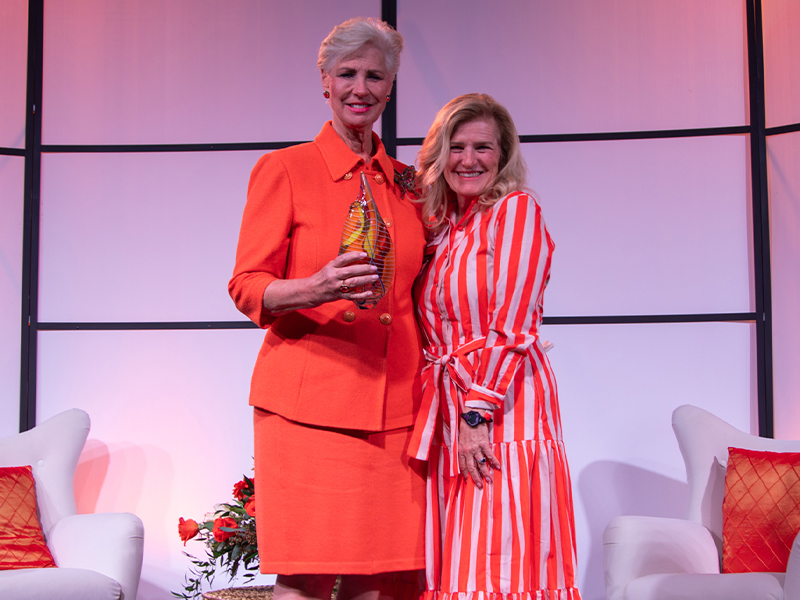 Two people stand together on a stage in front of a geometric backdrop, one holding a glass award, posed for a recognition moment at a Women for OSU event.