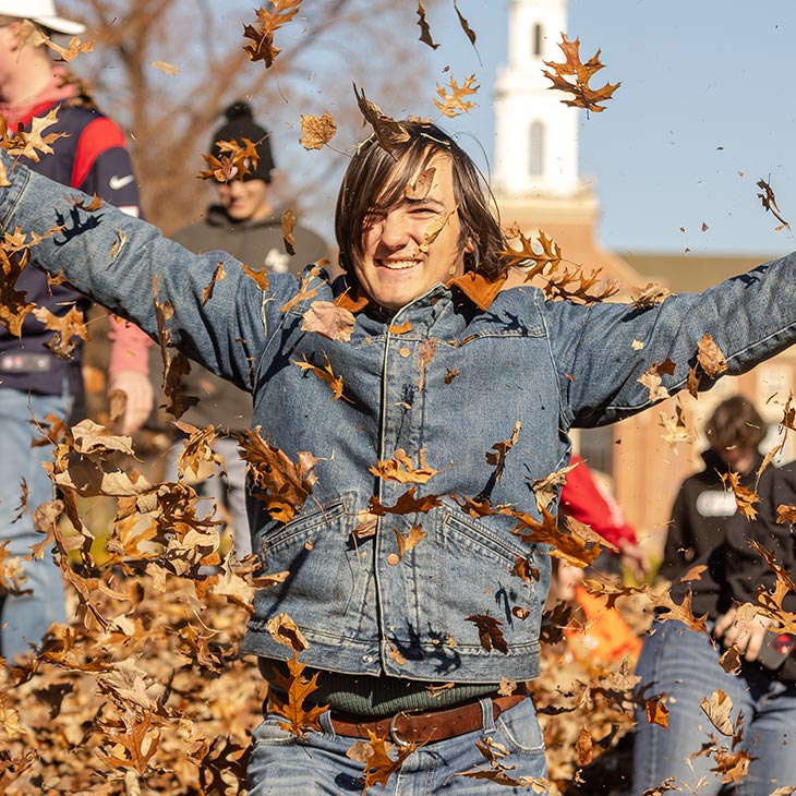 a male college student stands in front of a large leaf pile