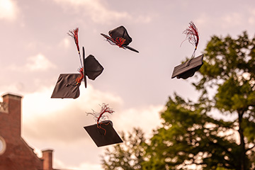 Black graduation caps with orange tassels fly through the air on the Oklahoma State University campus.