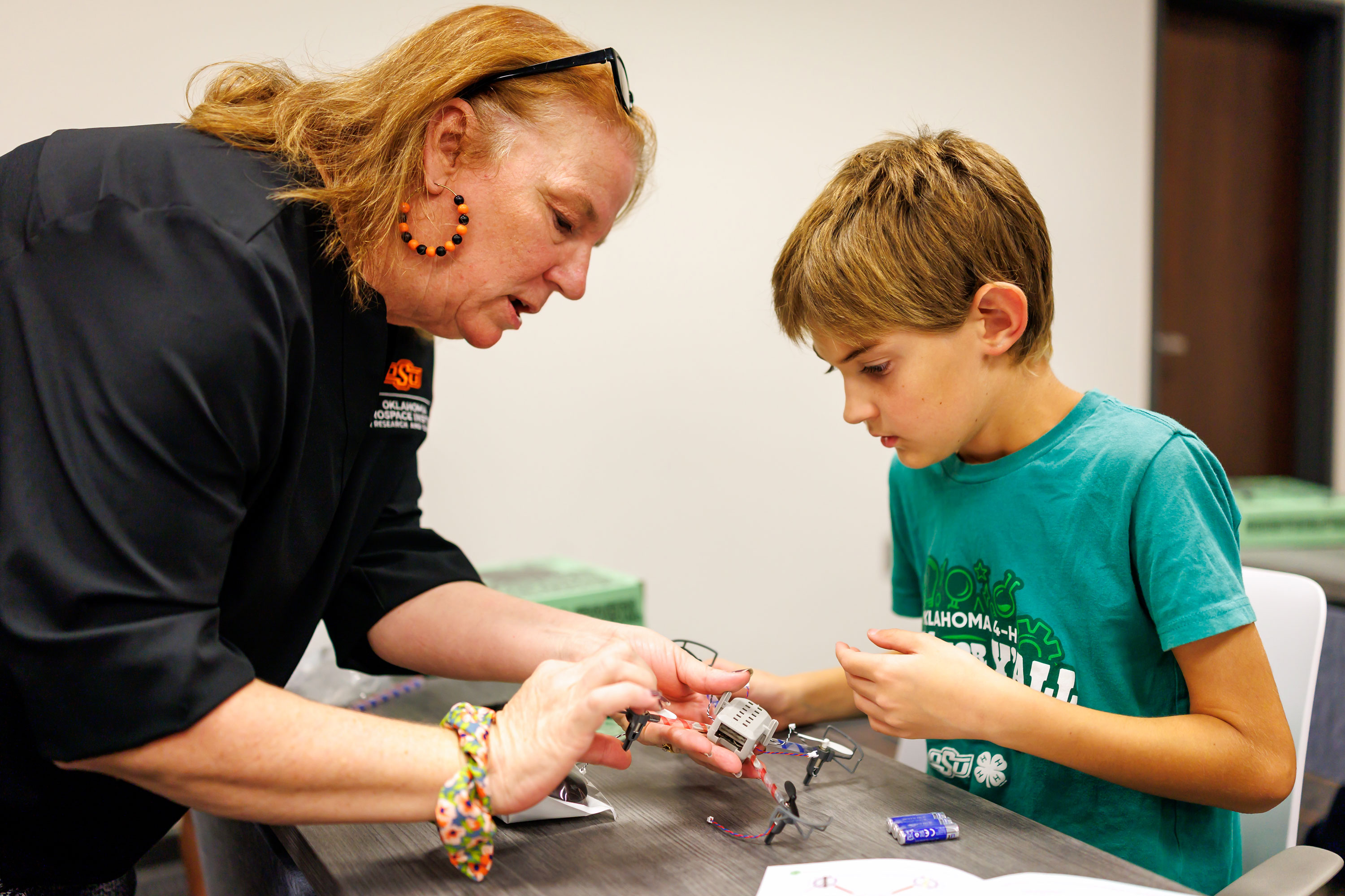 An adult helps an elementary student build a drone. 