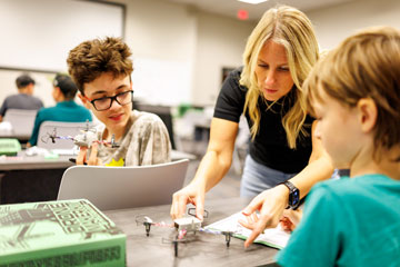 An adult show a student how to build a drone during a workshop