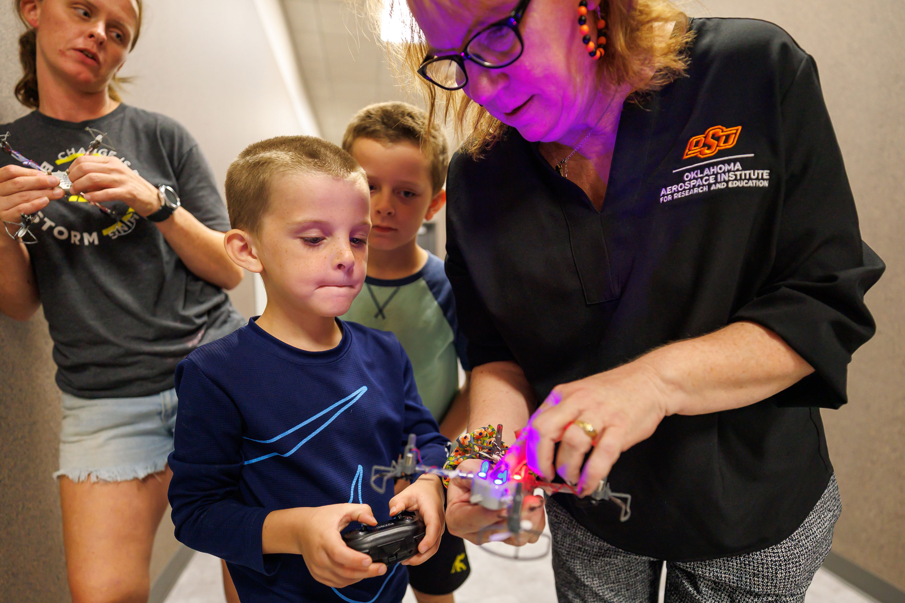 An adult helps an elementary student fly a drone. 