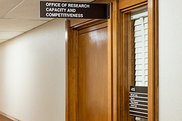 A hallway entrance with wood-framed doors and signage identifying the Office of Research Capacity and Competitiveness.