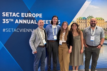 A group of five people standing in front of a poster for a research expo in Vienna.