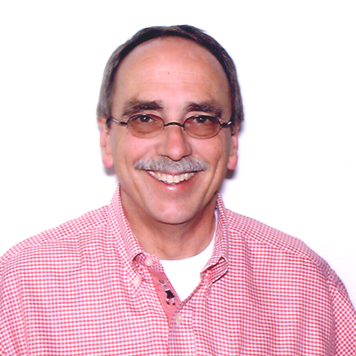 Head-and-shoulders portrait of a person wearing glasses and a red checkered shirt, facing the camera against a plain light background.