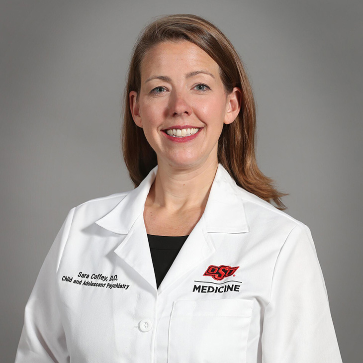 A person wearing a white OSU Medicine coat stands against a neutral background in a professional portrait setting.