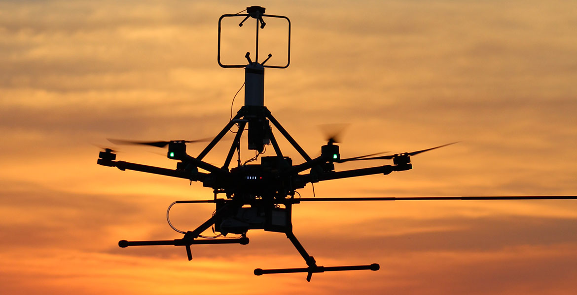 An unmanned aircraft flying in front of an orange sunset.
