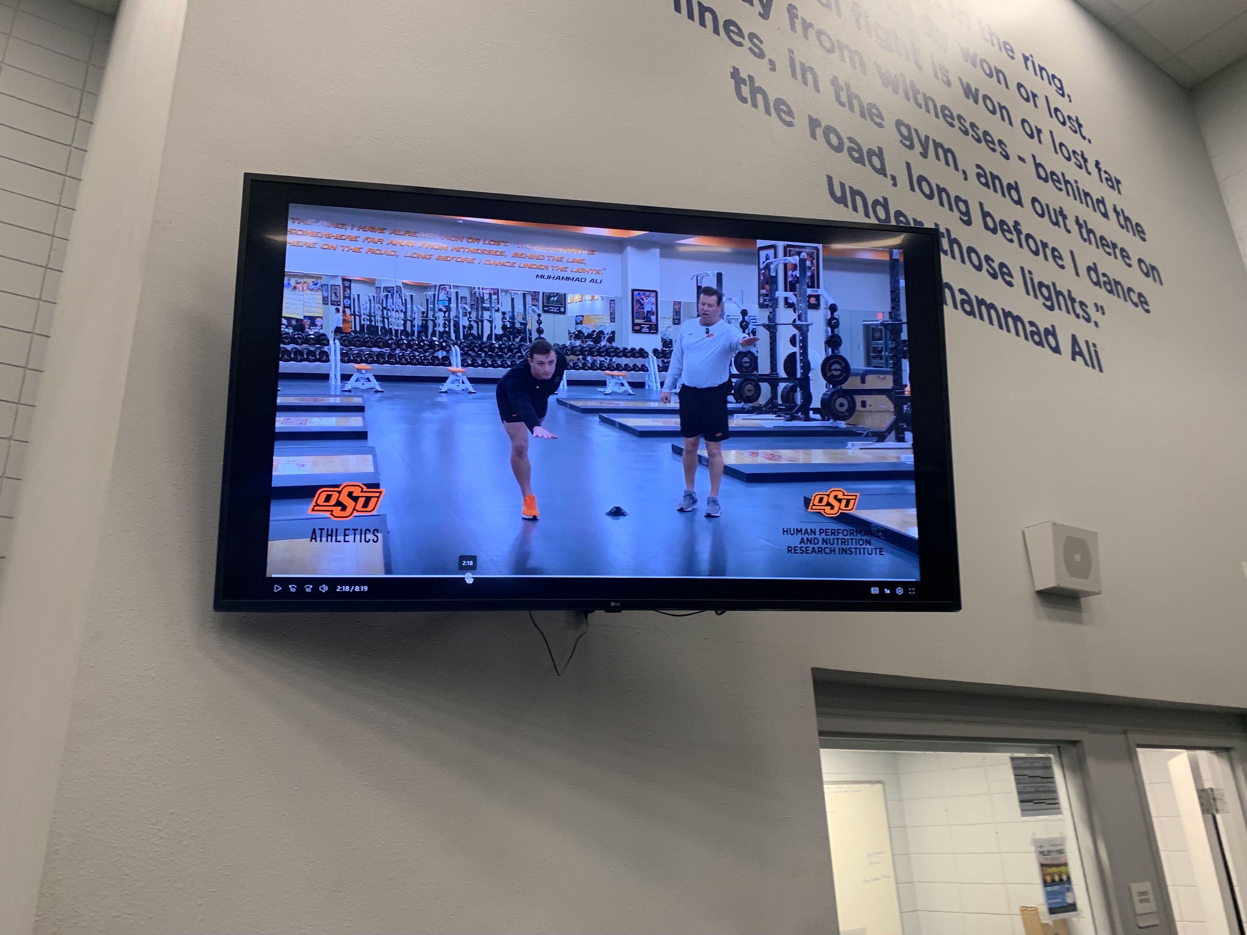 A TV screen shows a coach and student demonstrating a dynamic warm-up