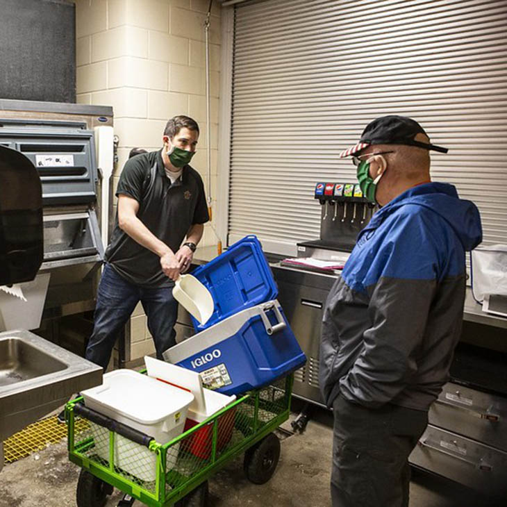 Tom Joyce (left), academic advisor, loads ice from Boone Pickens Stadium into coolers for a driver transporting COVID-19 samples. Joyce was instrumental in creating a custom courier service for sample pick-up and delivery.