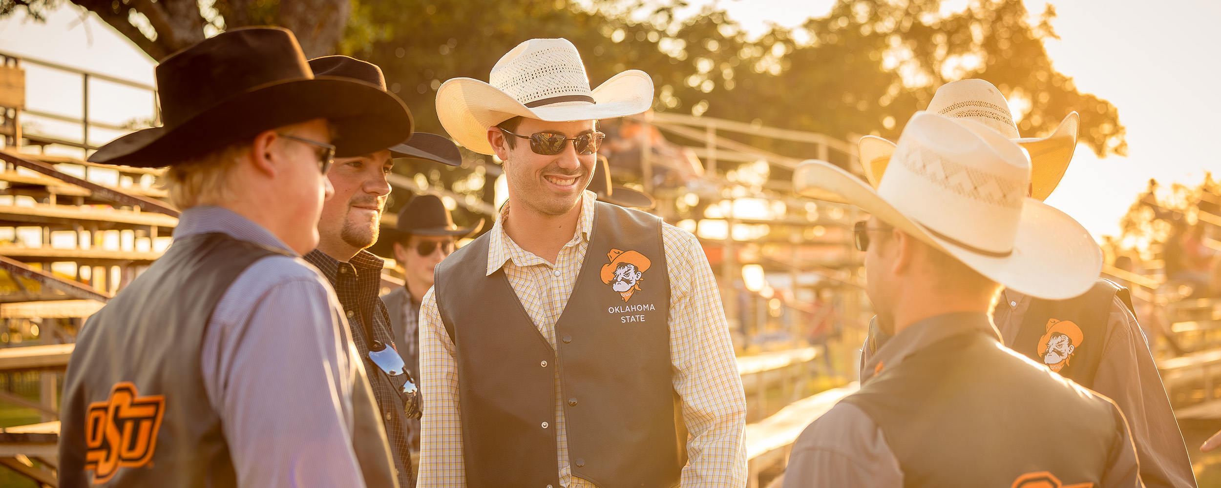 Three men wearing cowboy hats talk with a yellow sunset in the background.