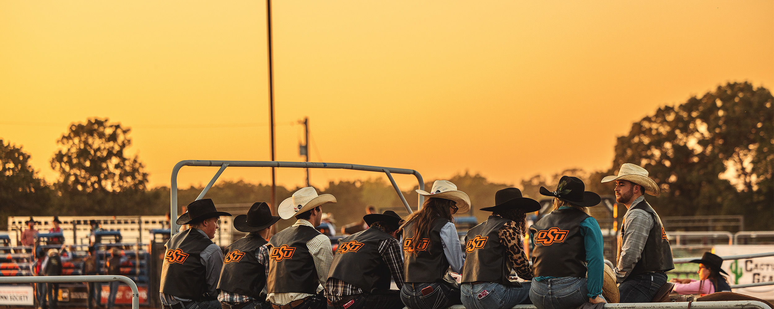 A group wearing cowboy hats talk with a yellow sunset in the background.