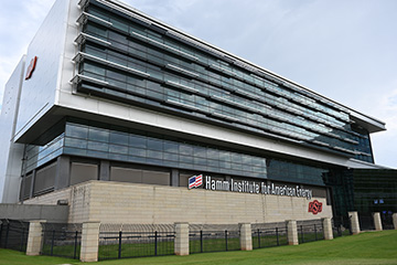 Exterior view of the Hamm Institute for American Energy building at Oklahoma State University, showcasing the modern glass-and-steel facility with prominent institute and OSU signage.