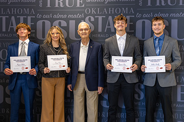 Five individuals pose in front of an Oklahoma State University backdrop, with four scholarship recipients holding certificates while standing beside an older presenter at an award recognition event.