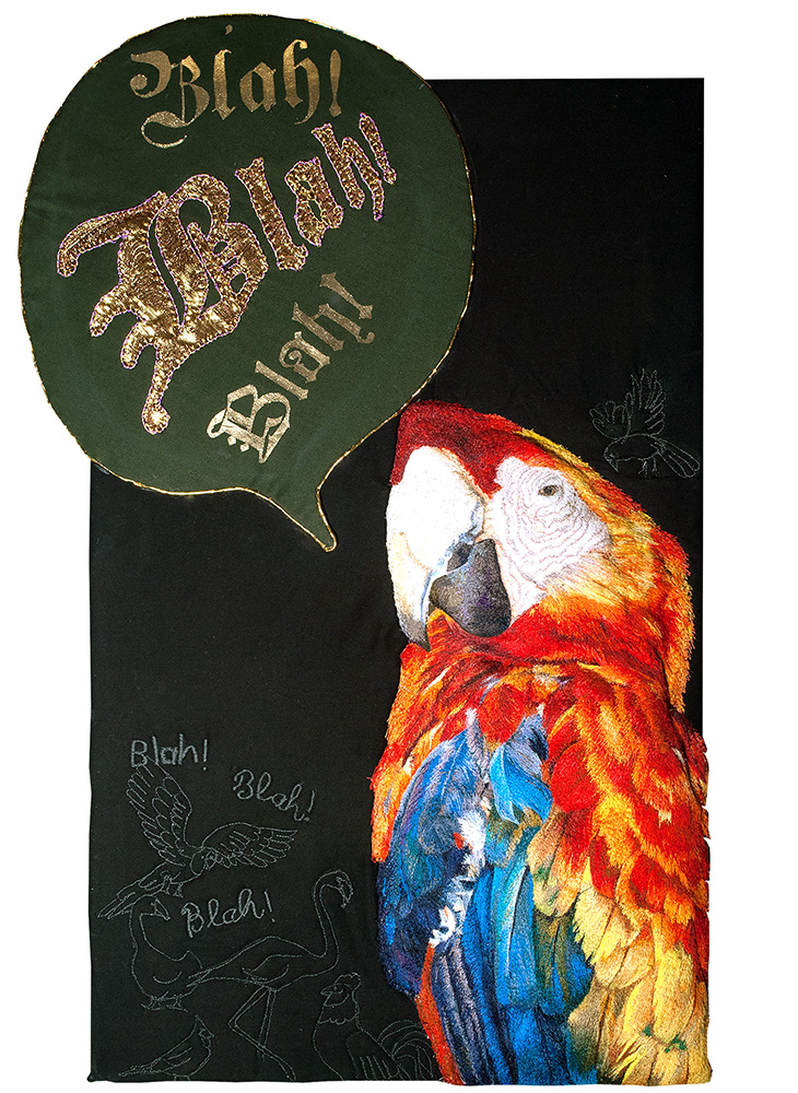 An embroidered artwork featuring a colorful parrot with vibrant red, yellow, and blue feathers on a black background. Above the parrot is a large speech bubble with the word 'Blah!' written three times in ornate gold lettering. Smaller embroidered birds surround the parrot, each with their own speech bubbles also containing the word 'Blah!'