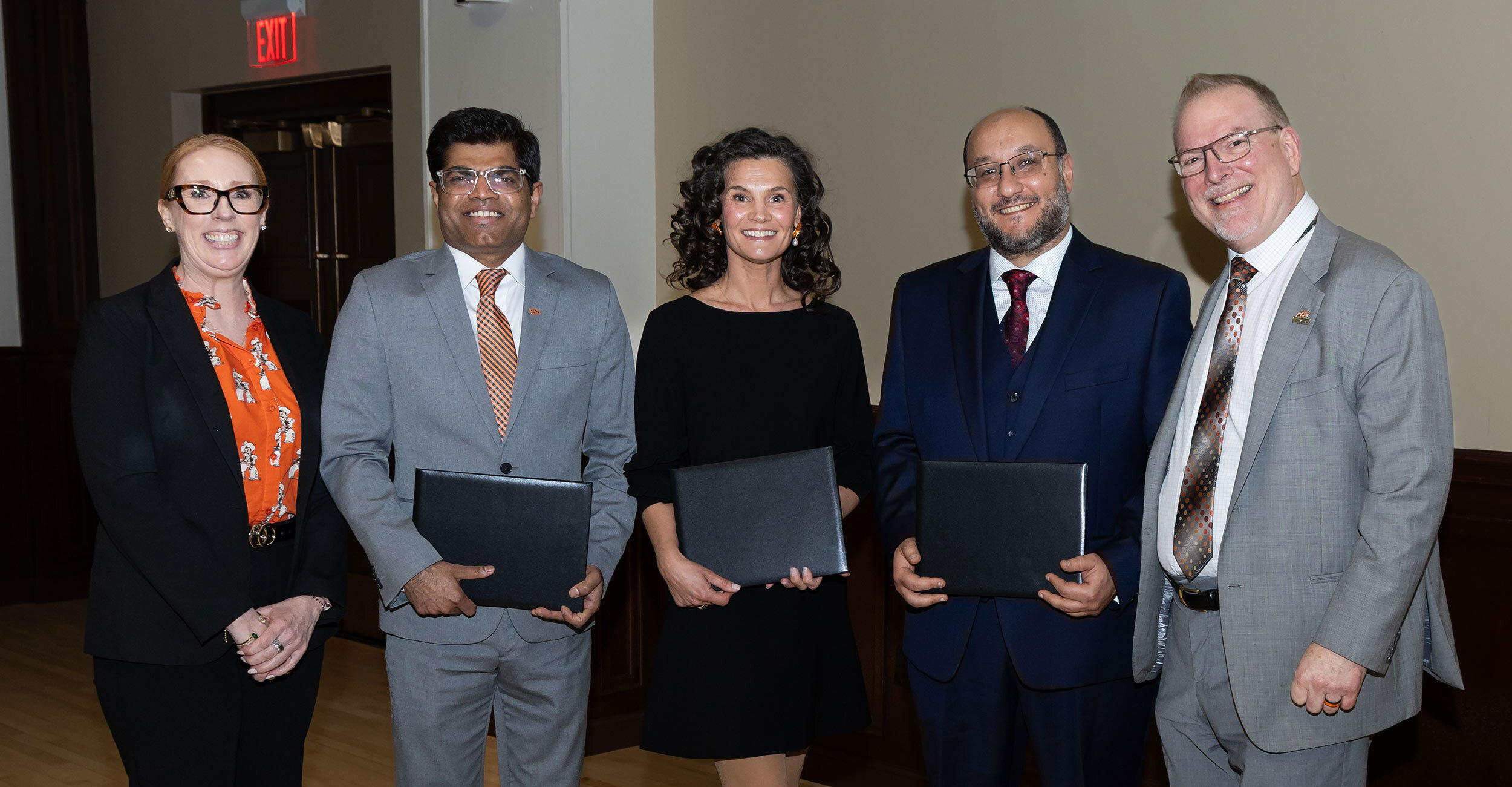 Five individuals stand together holding certificates in a formal indoor setting, suggesting recognition at an academic or research awards reception.