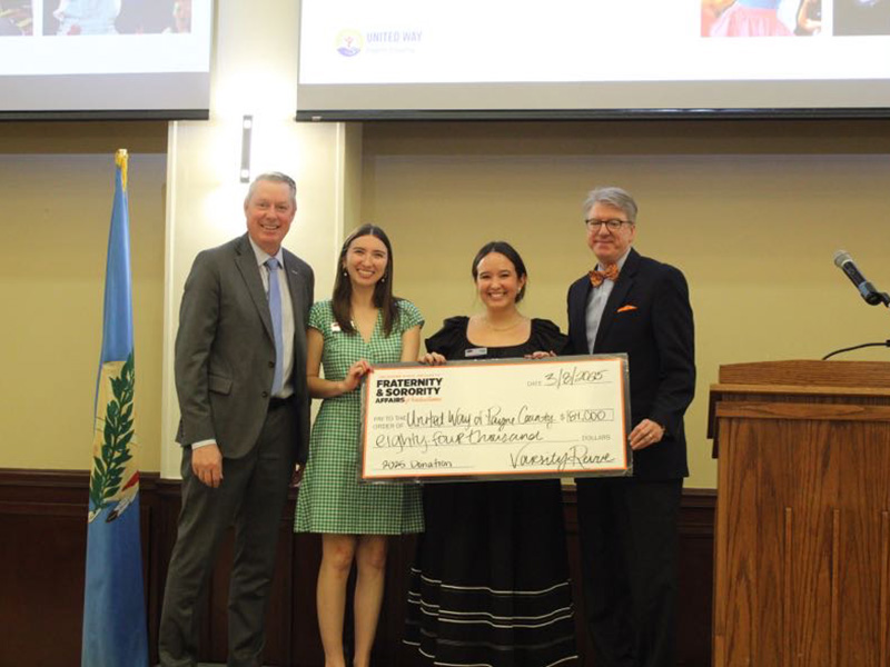 Four people standing indoors holding a large ceremonial check made out to 'United Way of Payne County' for $84,000, dated 3/26/2025.