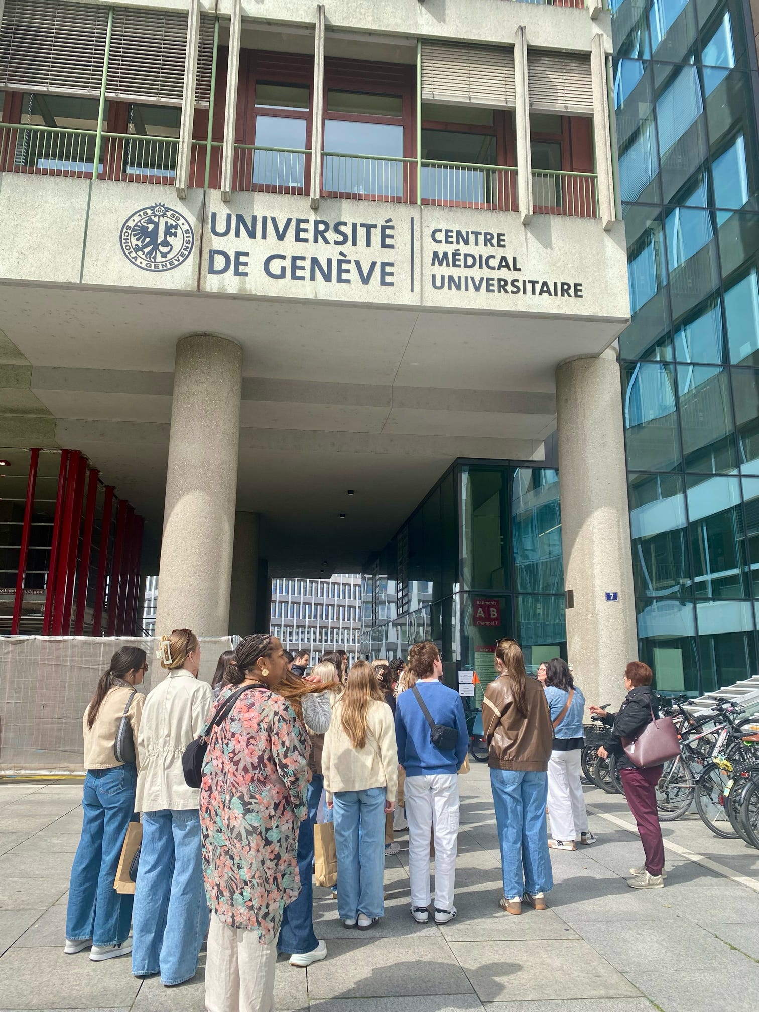 Students stand outside a modern university medical building near its main entrance.