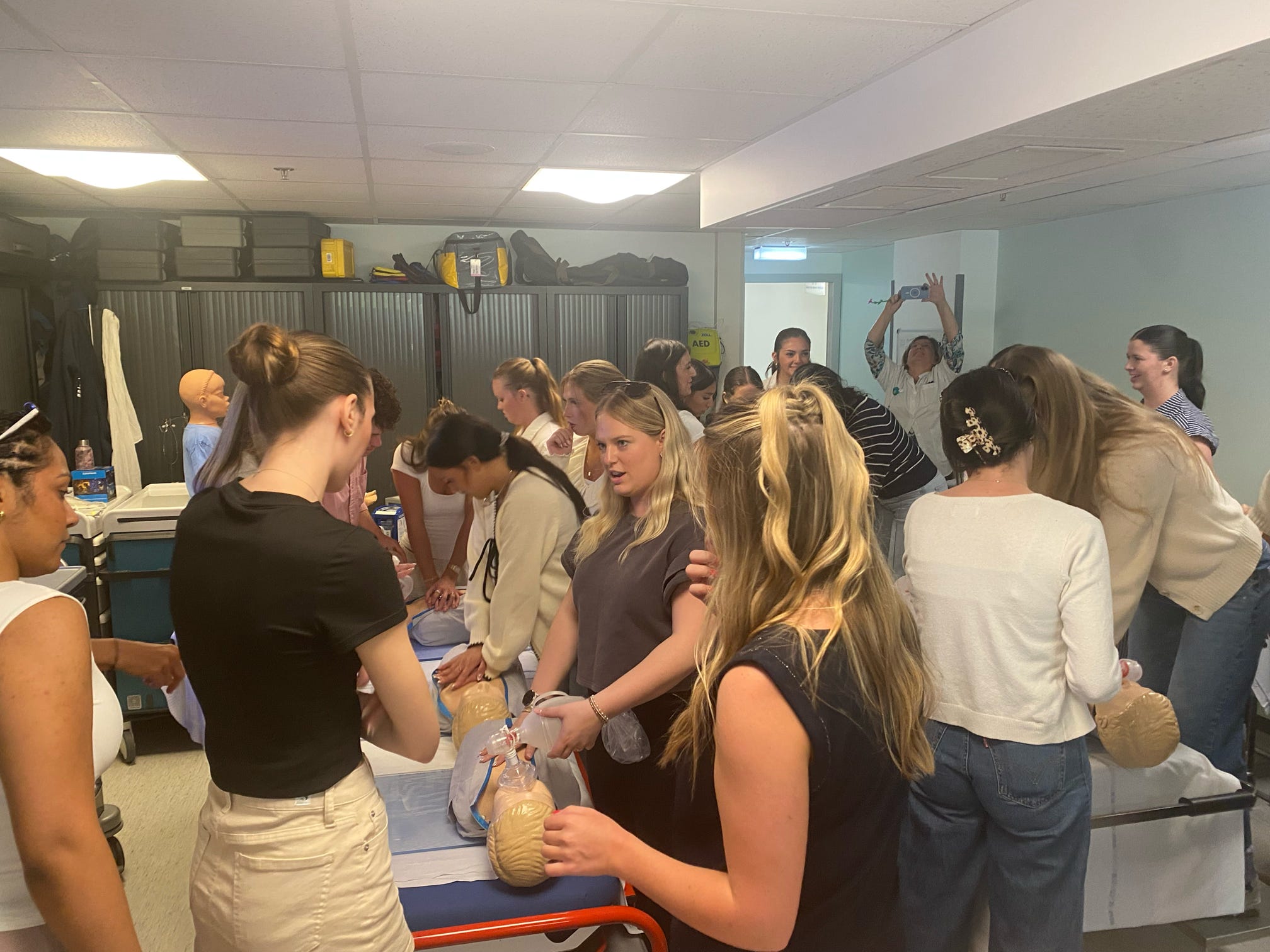Students practice CPR on medical training mannequins in a classroom equipped with simulation equipment.