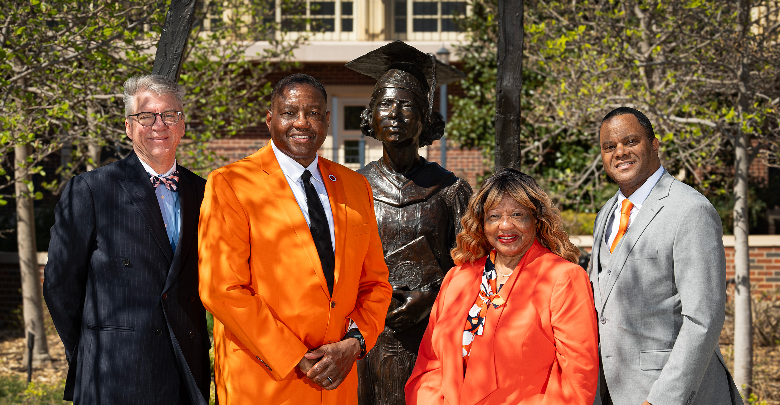 Five university leaders pose outdoors beside a bronze statue on the Oklahoma State University campus, marking a formal recognition or commemorative event.