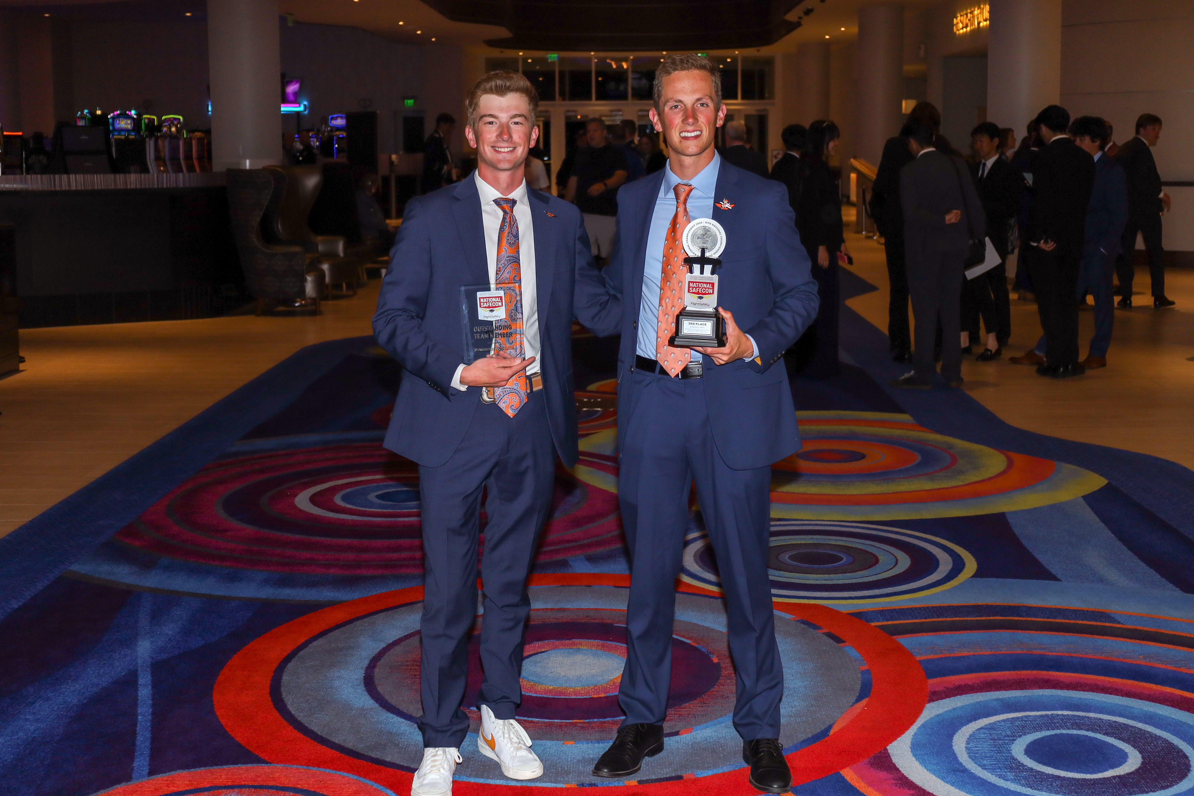 Nathan Leech and Tanner Trout smile wearing blue suits holding trophies from their awards 
