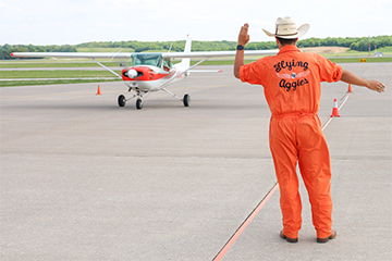 Member of the Flying Aggies walks backward directing plane on tarmac
