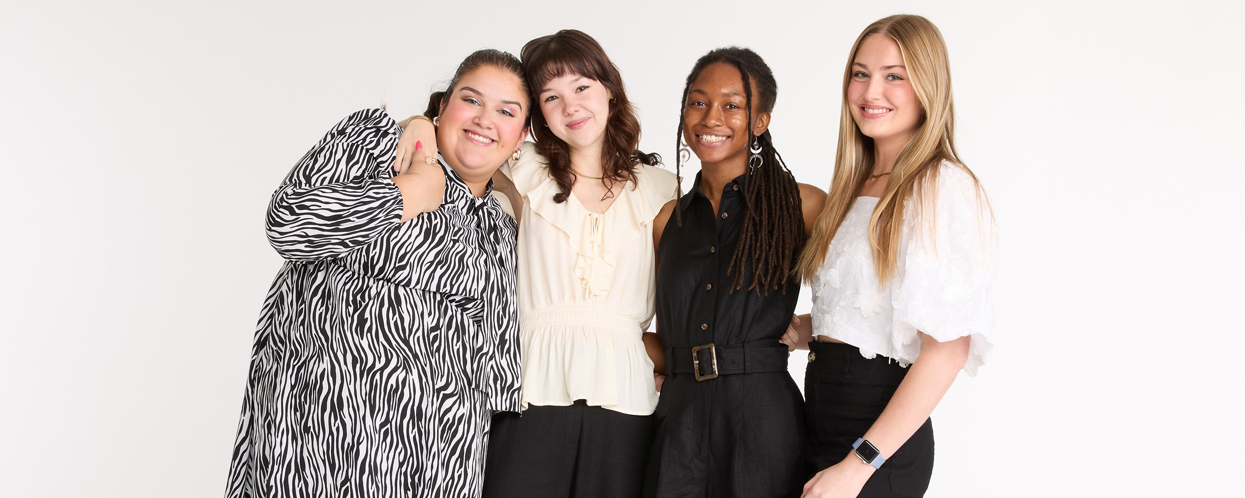 Four people stand closely together against a white background, posing side by side in coordinated professional‑casual outfits for a group portrait.