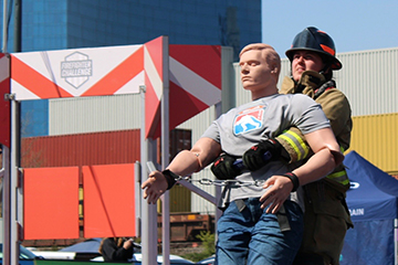Hannah Marie Akoury drags a life‑sized rescue mannequin across a padded course during a firefighter challenge event.