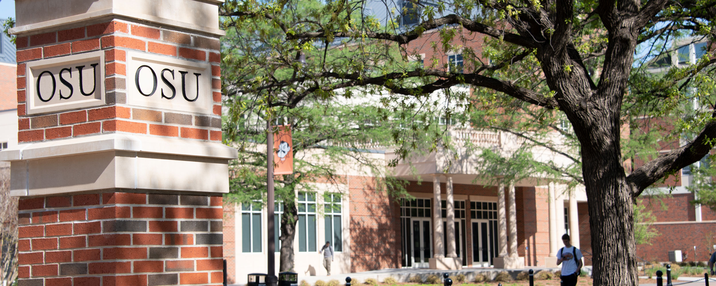 A pillar spells out OSU while a tree and building sit in the background.