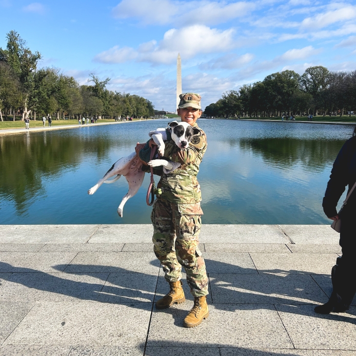 Tina Sergi in her military uniform, holding her dog, in front of the Washington Monument