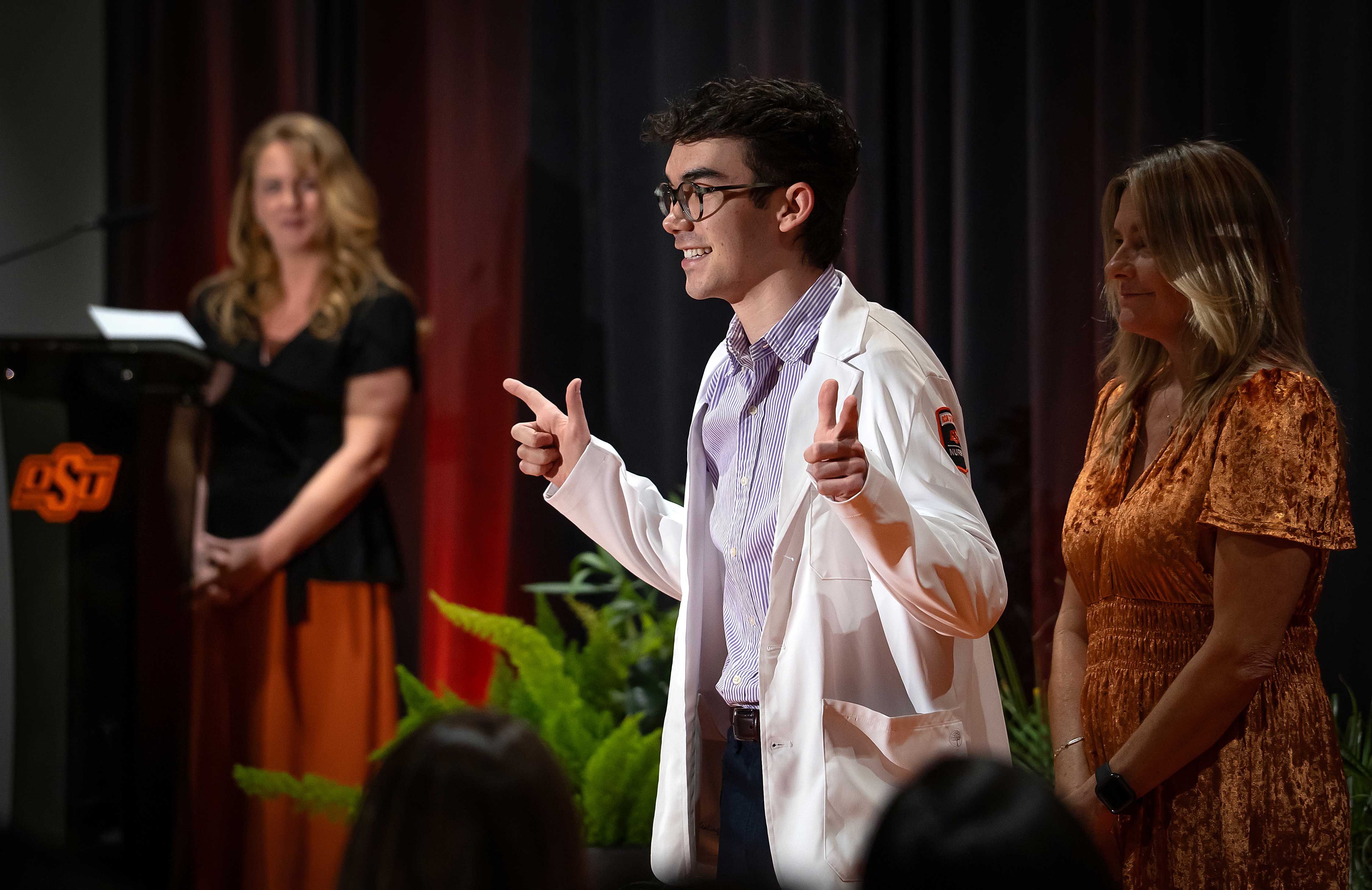 BSN student on stage after receiving white coat during ceremony.