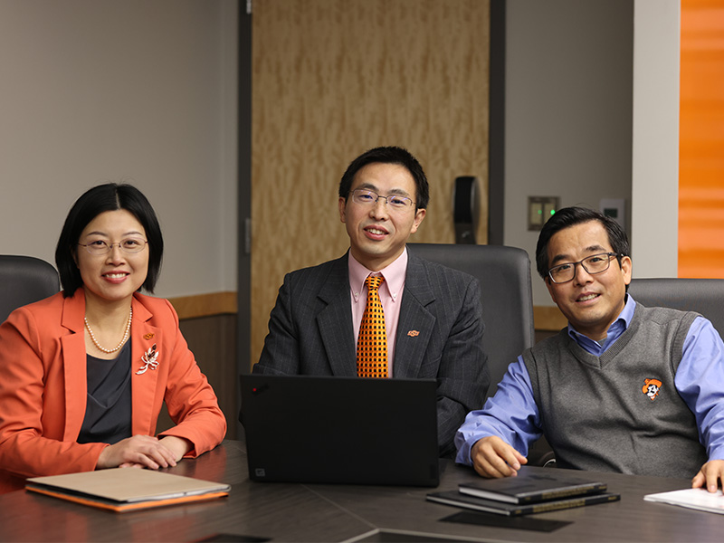 The three researchers working on this project sit around the corner of a conference table with laptops, folders and books in front of them.