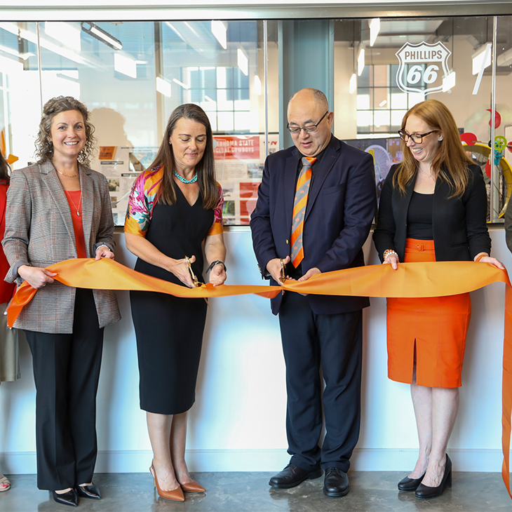 Four people cut an orange ribbon
