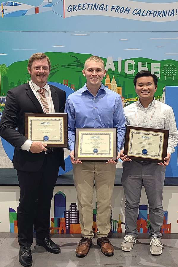 Three men proudly display their certificates in front of a wall.