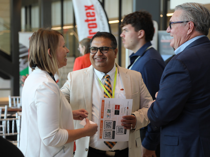 Hosts and attendees of conference stand together discussing and smiling.