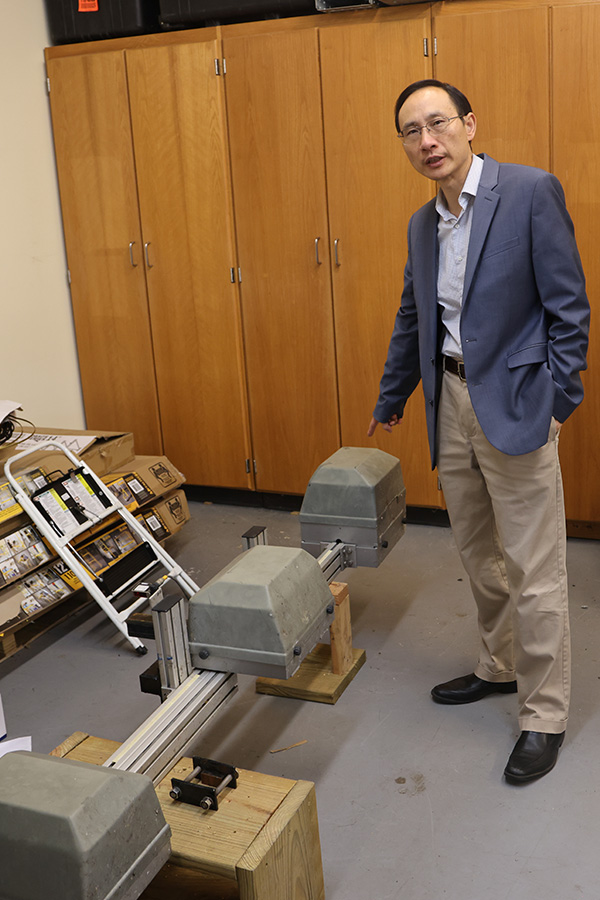 A man wearing a suit explains a large piece of equipment as he points to it.