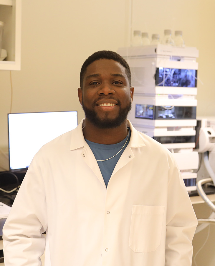 A man in a lab coat stands before a computer, symbolizing a commitment to scientific inquiry and technological advancement.