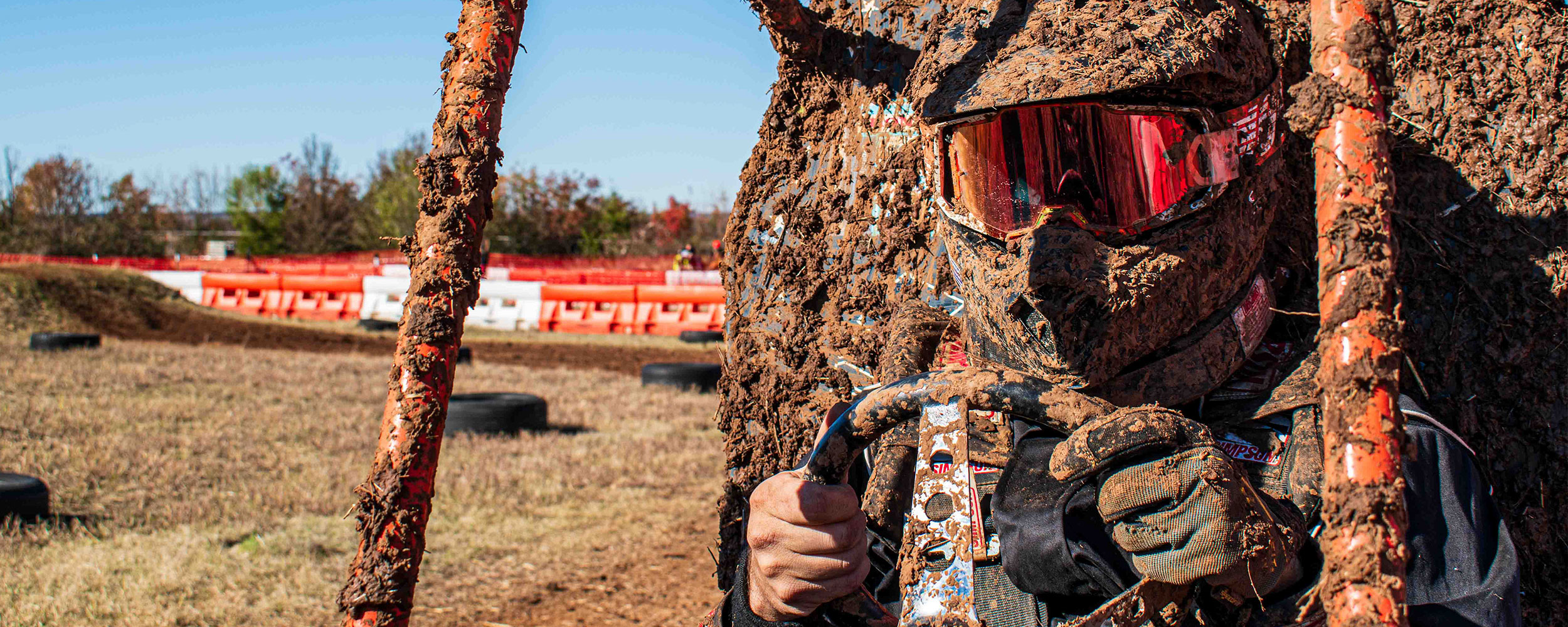OSU Cowboy Racing team member and race car coated in mud with race track in the background