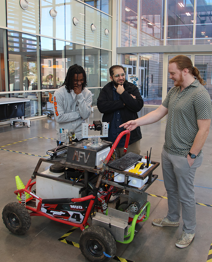 A diverse group of individuals gathered around a parked vehicle, engaged in conversation and observation.