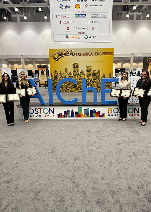 A group of OSU students hold their awards in front of a display for the AIChE Student Design contest.