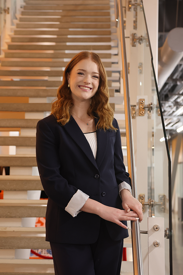 A woman is dressed up and standing on a staircase while smiling in a portrait photo.