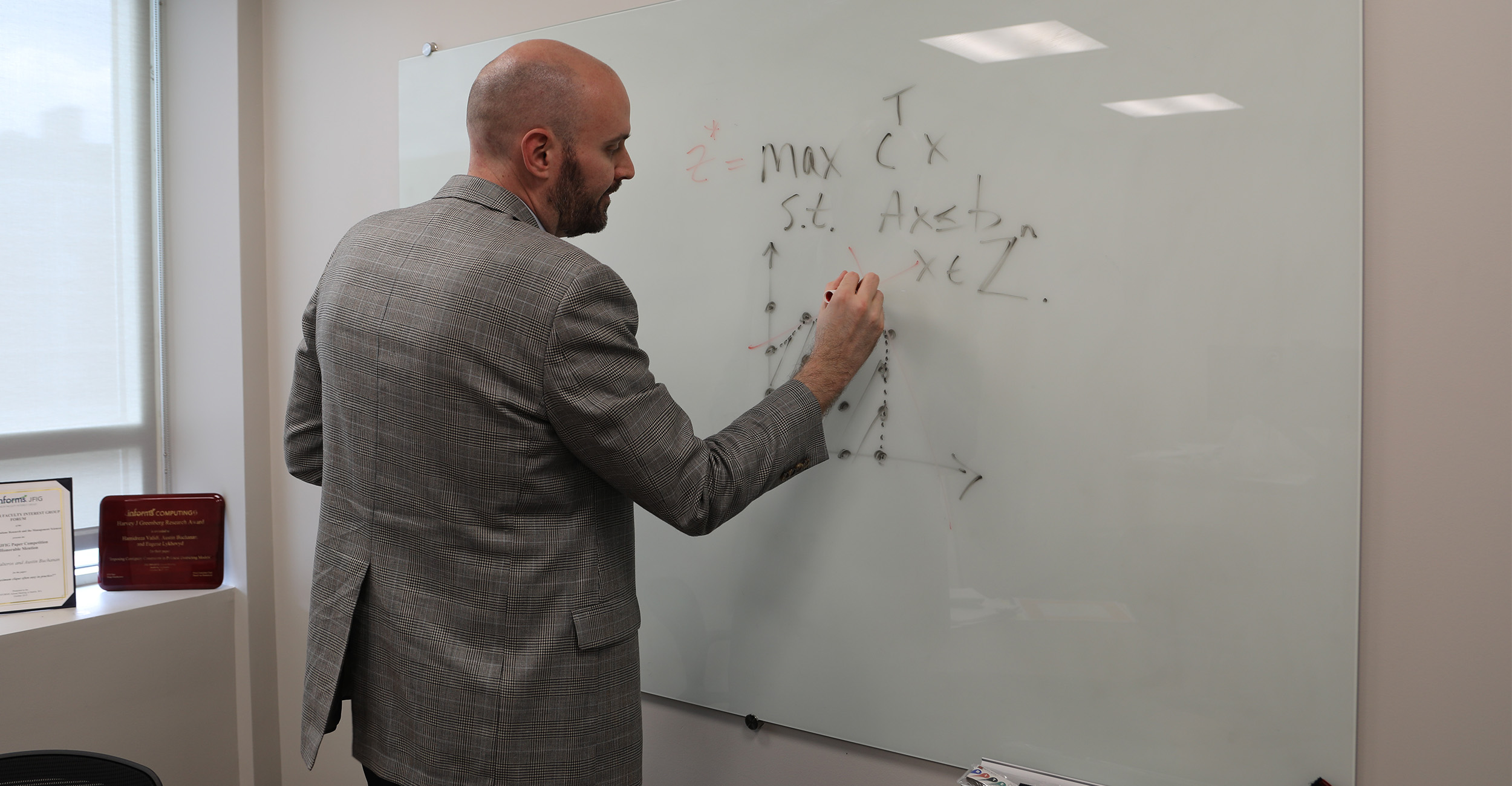 Dr. Austin Buchanan, a professor in the OSU School of Industrial Engineering and Management, writes an equation on the white board in his office.
