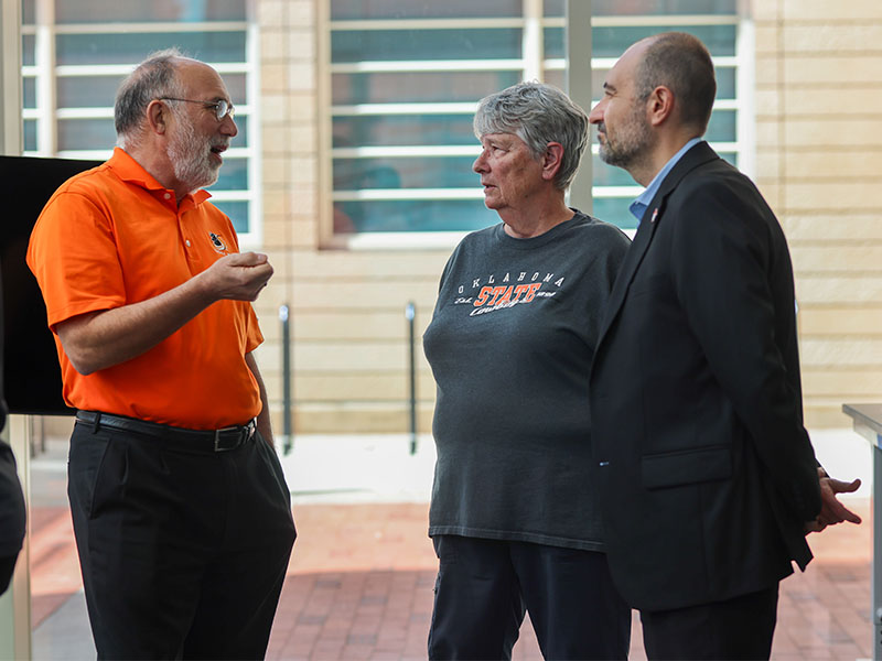 Mary Davey stands talking to two men- one dressed in an orange OSU shirt and the other in a suit.