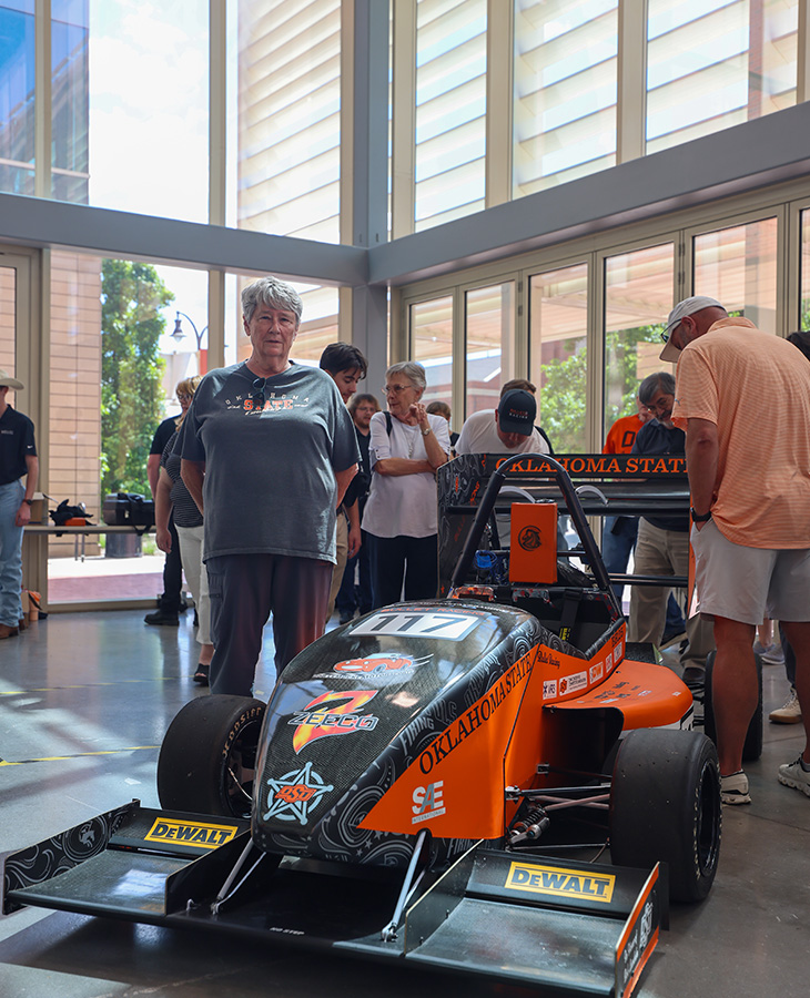 A woman stands beside an orange and black formula racing car.