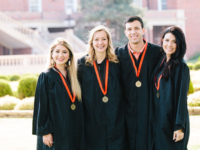 Four individuals pose for a photo in their black graduation gowns.
