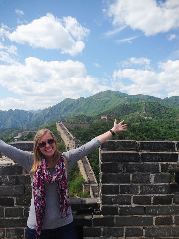 A happy individual stands with hands raised up in a Y infront of a captivating landscape.
