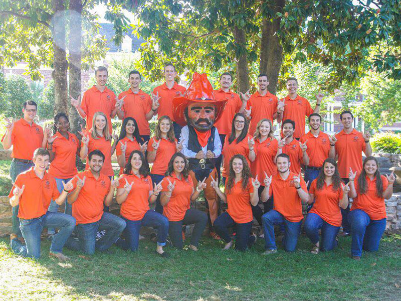 A group of college students all wearing an orange shirt pose for a group picture with Pistol Pete.