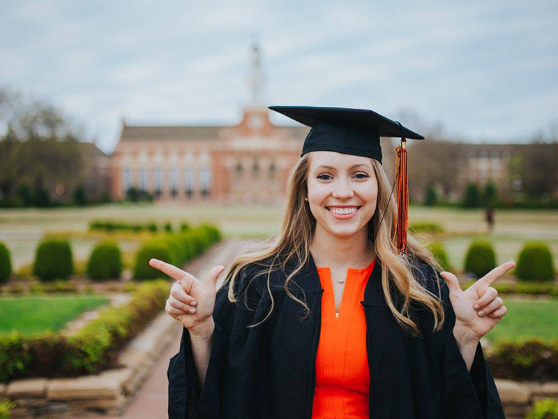 An OSU graduate poses in a cap and gown in front of Edmon Low.