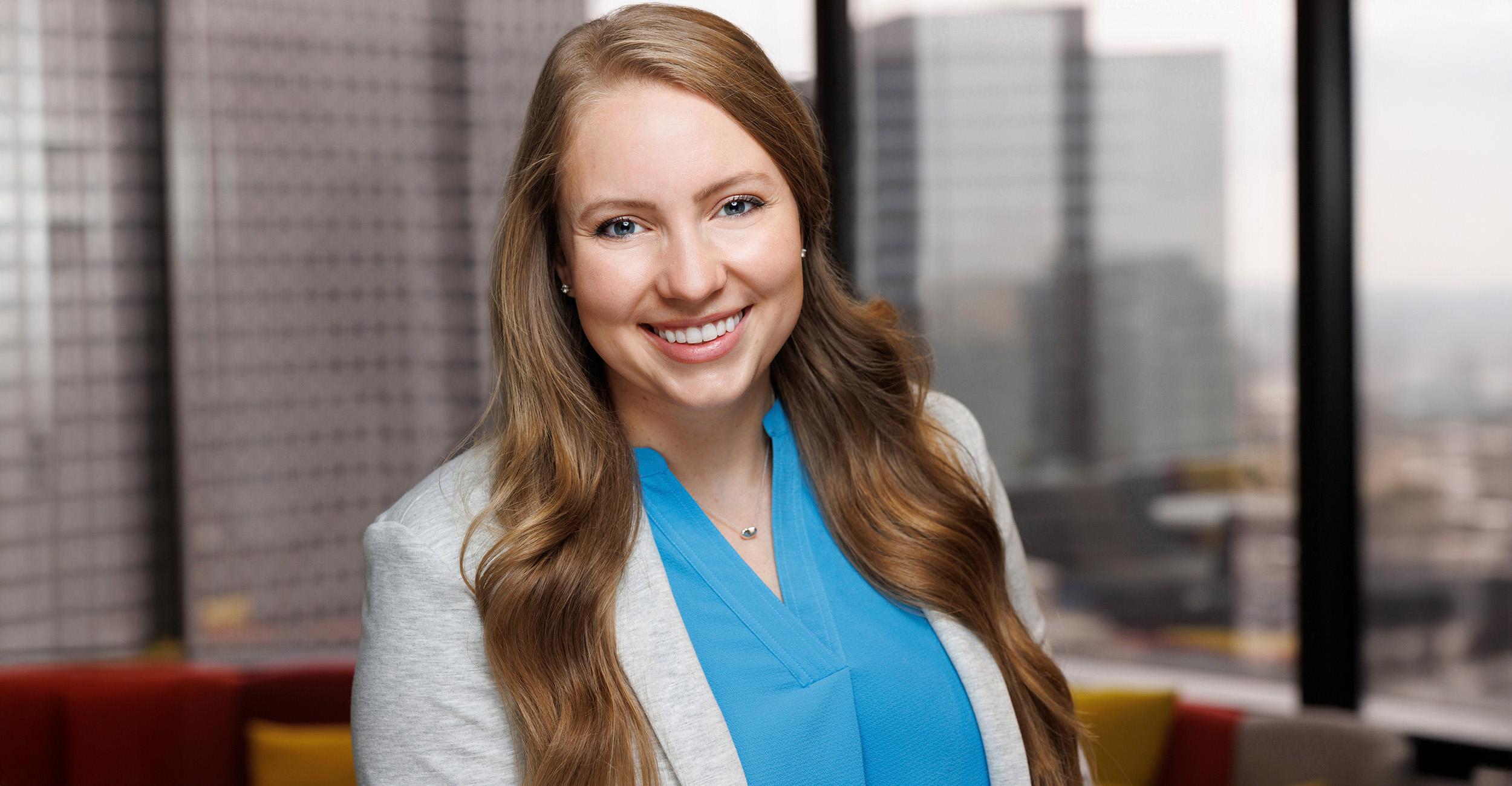 A young woman dressed in business attire poses for a headshot against a skyscraper with a city skyline in the background.